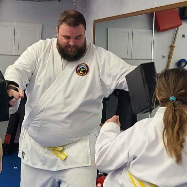 Sensei Kyra kneeling to award belt stripes to a young karate student, capturing the mentorship and care at the heart of Colorado Karate Club